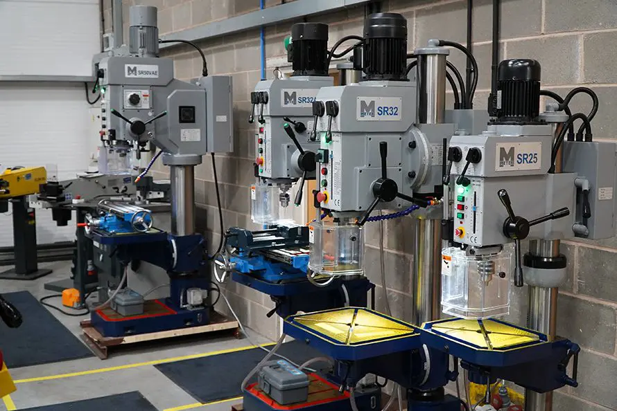 Line-up of Meyer metalworking machinery including pillar drills, with some other brand belt grinders in the background, arranged in a bright showroom with a clean white background."