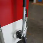 Close-up of a manual hydraulic hand pump with a long silver lever and black grip, mounted to the side of a red and white industrial machine