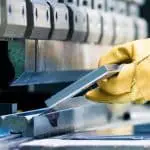 Image of gloved hands holding a piece of metal on a pressbrake