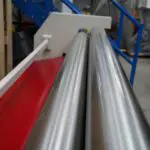 Looking down the length of a set of polished sheet rolls, the frame of the machine is visible, with a staircase in the distant distance.