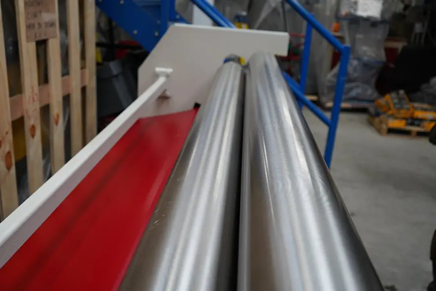 Looking down the length of a set of polished sheet rolls, the frame of the machine is visible, with a staircase in the distant distance.