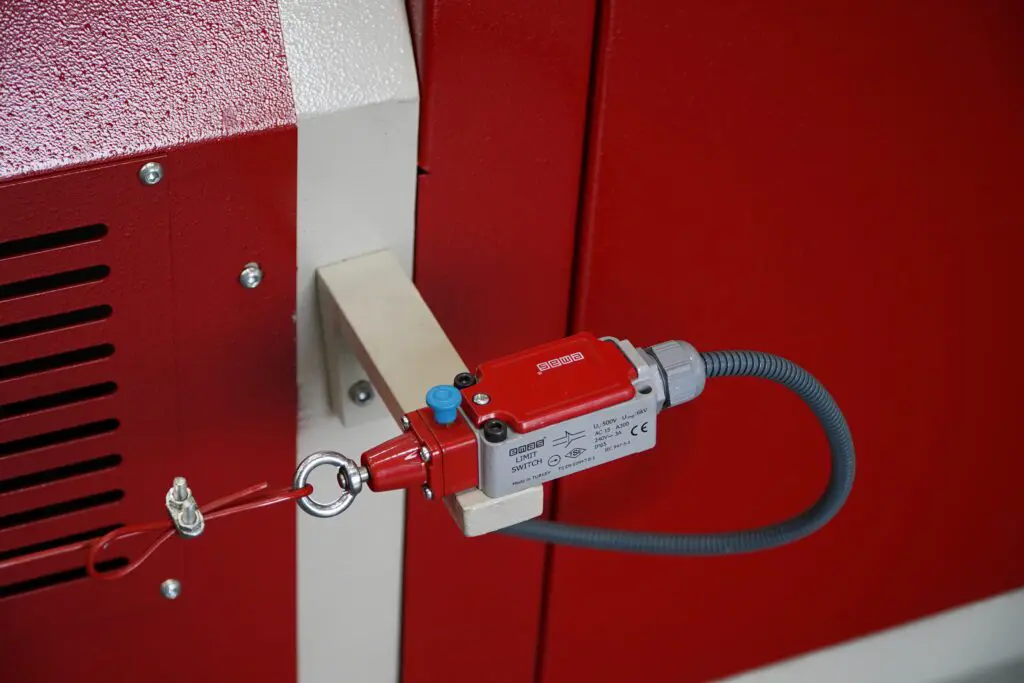 Close-up of a pull-cord emergency stop switch on a red machine, featuring a red EMAS limit switch connected to a safety wire