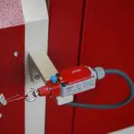 Close-up of a pull-cord emergency stop switch on a red machine, featuring a red EMAS limit switch connected to a safety wire