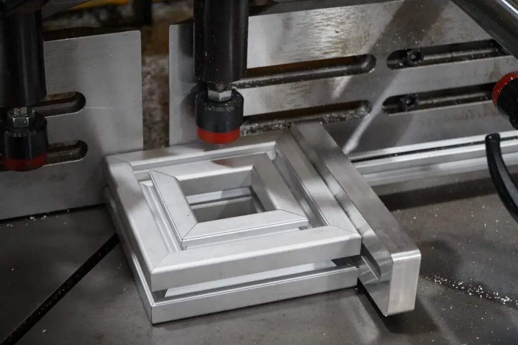 Close-up of aluminium extrusion profiles being processed on a specialized cutting or mitring machine