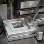 Close-up of aluminium extrusion profiles being processed on a specialized cutting or mitring machine