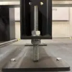 Close-up of an adjustable leveling foot for a machine frame, featuring a threaded bolt with locking nuts to precisely set the height of a vertical steel support
