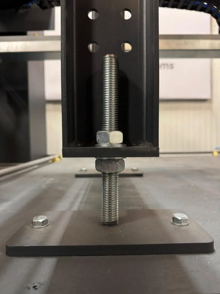 Close-up of an adjustable leveling foot for a machine frame, featuring a threaded bolt with locking nuts to precisely set the height of a vertical steel support