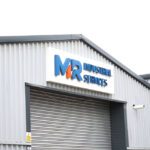 MR Industrial Services Logo on a pitched roof steel building, with a roller track door